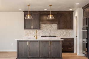 Kitchen with dark brown cabinetry, backsplash, appliances with stainless steel finishes, light wood finished floors, and recessed lighting