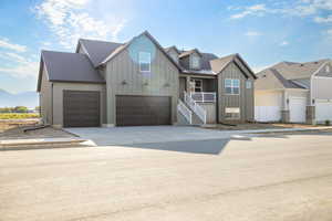 View of front of home with board and batten siding, concrete driveway, a shingled roof, and stairway