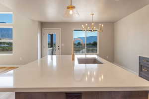 Kitchen featuring a center island with sink, light stone countertops, pendant lighting, and a chandelier