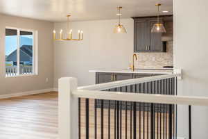 Kitchen featuring decorative backsplash, decorative light fixtures, light wood-style flooring, light stone counters, and a chandelier