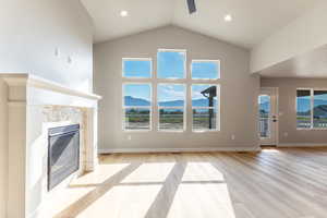 Unfurnished living room with a mountain view, a stone fireplace, light wood finished floors, ceiling fan, and high vaulted ceiling