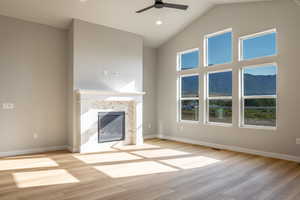 Unfurnished living room with a mountain view, high vaulted ceiling, a premium fireplace, a ceiling fan, and light wood-type flooring