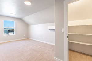 Bonus room with light colored carpet, vaulted ceiling, a textured ceiling, and a wall mounted air conditioner
