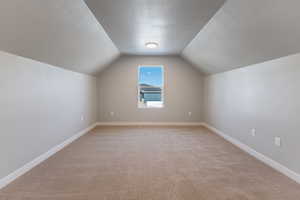 Bonus room with light carpet, a textured ceiling, and lofted ceiling