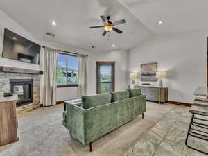 Living room featuring lofted ceiling, ceiling fan, light carpet, recessed lighting, and a stone fireplace