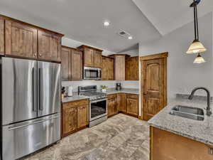 Kitchen featuring stainless steel appliances, decorative light fixtures, light stone counters, brown cabinets, and recessed lighting
