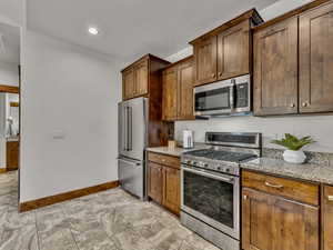 Kitchen with stainless steel appliances, light stone counters, recessed lighting, and brown cabinets