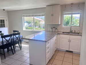 Kitchen with white cabinetry, decorative backsplash, light tile patterned floors, and a peninsula