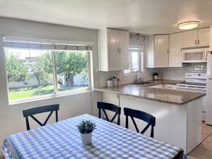 Kitchen with white cabinetry, backsplash, white appliances, a kitchen breakfast bar, and a textured ceiling