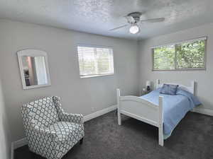 Bedroom with a textured ceiling, dark colored carpet, and a ceiling fan