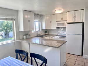 Kitchen featuring white appliances, white cabinets, light stone countertops, decorative backsplash, and a textured ceiling