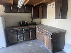 Kitchen with dark brown cabinetry, unfinished concrete flooring, and freestanding refrigerator