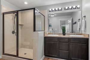 Full bath with a shower stall, a textured ceiling, double vanity, light wood-style flooring, and recessed lighting