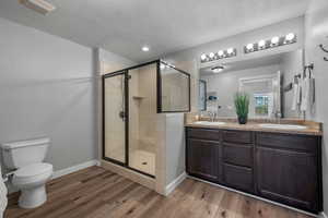 Bathroom featuring a stall shower, light wood-type flooring, double vanity, and a textured ceiling