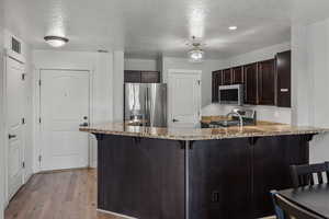 Kitchen featuring a kitchen bar, dark brown cabinetry, a peninsula, a textured ceiling, and appliances with stainless steel finishes