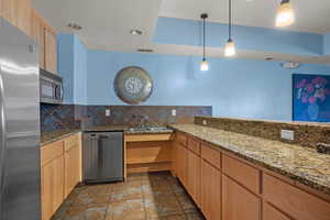 Kitchen featuring light brown cabinets, stainless steel appliances, hanging light fixtures, light stone counters, and a textured ceiling