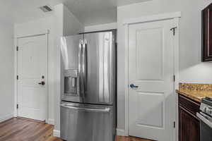 Kitchen with stainless steel fridge, light stone counters, dark brown cabinets, light wood-style floors, and a textured ceiling