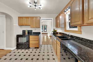 Kitchen featuring arched walkways, black appliances, black granite counters, and light floors