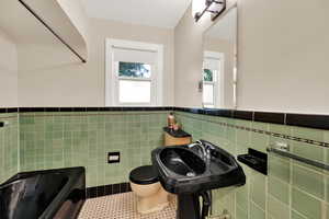 Bathroom with a tub, and shower patterned floors, tile walls, and wainscoting