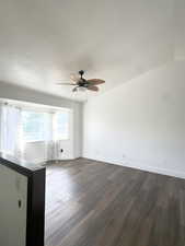 Unfurnished living room featuring dark wood-type flooring, a ceiling fan, and a textured ceiling