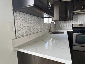 Kitchen with gas range, backsplash, light stone countertops, and under cabinet range hood