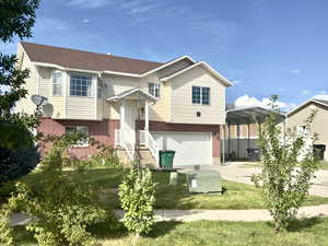 View of front facade with brick siding, driveway, a detached carport, an attached garage, and a front lawn