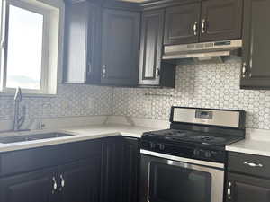 Kitchen with stainless steel gas stove, decorative backsplash, under cabinet range hood, and light stone counters