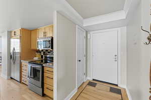 Kitchen featuring appliances with stainless steel finishes, light wood finished floors, tasteful backsplash, and light brown cabinetry
