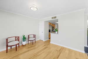 Sitting room with ornamental molding and light wood-style floors