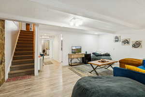 Living area featuring stairway, light wood-type flooring, and beam ceiling
