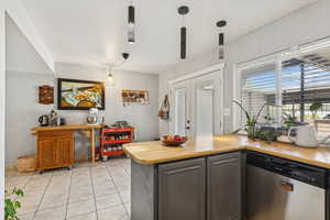 Kitchen featuring dishwasher, light tile patterned floors, decorative light fixtures, wood counters, and a peninsula