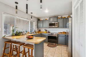 Kitchen featuring a peninsula, gray cabinets, a breakfast bar area, and appliances with stainless steel finishes