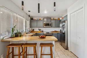 Kitchen with pendant lighting, light countertops, stainless steel appliances, gray cabinetry, and a breakfast bar area