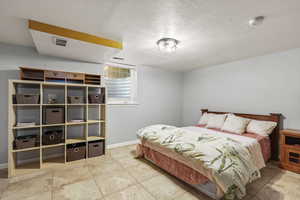 Large bedroom featuring textured ceiling and light tile flooring.