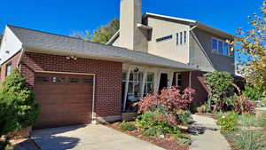 View of front of property featuring brick siding, covered porch, an attached garage, driveway stucco siding