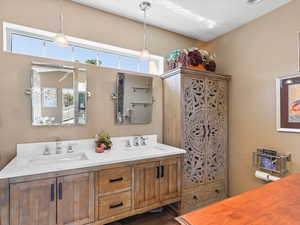 Primary Bathroom with double vanity, hand-carved amoire, and light tile flooring.