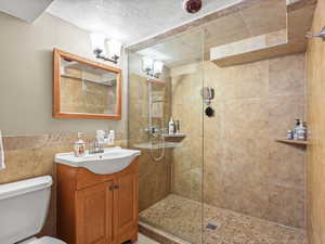 Large bathroom featuring vanity, tile walls, tile floors, walk-in shower, a textured ceiling, and a linen closet.