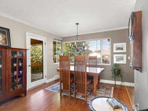 Dining area with oak floors, a chandelier, plenty of natural light, and ornamental molding.