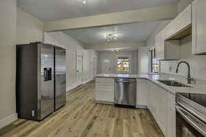 Kitchen featuring appliances with stainless steel finishes, light wood-style flooring, a peninsula, white cabinetry, and light stone countertops