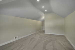 Additional living space with lofted ceiling, light colored carpet, and recessed lighting