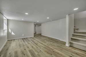 Below grade area featuring stairway, light wood-style flooring, a textured ceiling, and recessed lighting