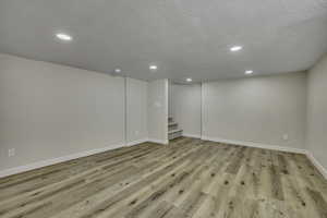 Finished below grade area with light wood-type flooring, recessed lighting, a textured ceiling, and stairs