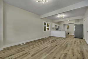 Unfurnished living room with beam ceiling, light wood-style floors, a chandelier, and a textured ceiling