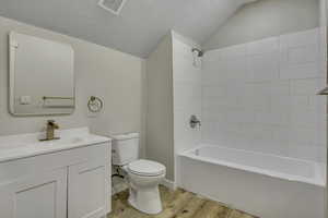 Full bath featuring a textured ceiling, light wood-style floors,  shower combination, vanity, and lofted ceiling