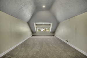 Bonus room featuring a textured ceiling, light carpet, and lofted ceiling
