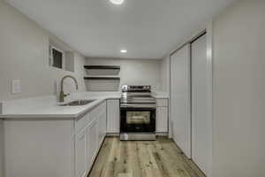 Kitchen with open shelves, stainless steel electric stove, white cabinetry, light wood-type flooring, and light stone counters