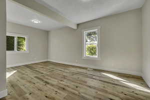 Unfurnished room with beamed ceiling, light wood-style floors, and healthy amount of natural light