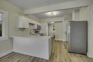 Kitchen featuring appliances with stainless steel finishes, white cabinetry, a peninsula, light wood-style floors, and light stone counters