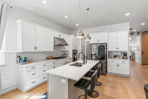 Kitchen with a breakfast bar, hanging light fixtures, a center island with sink, appliances with stainless steel finishes, and light wood-style floors