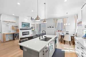 Kitchen featuring light wood-style floors, pendant lighting, an island with sink, open floor plan, and wood walls
